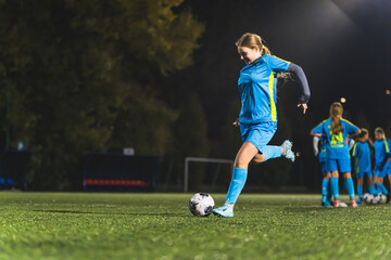 Naklejka premium little girl practicing in scoring a goal at the soccer practice, footballer girls with blue uniforms. High quality photo