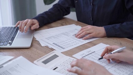 Close up of professional hands using a calculator to conduct financial analysis at the background of a colleague with a magnificent glass. Bookkeeping, finance audit and taxes