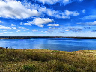 Tranquil lakeside view with grassy hillside under a clear blue sky in the afternoon