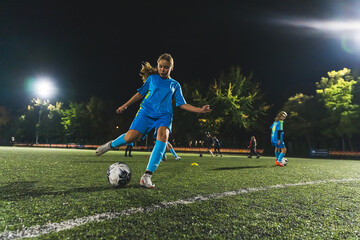 soccer player girl with long hair kicking a ball at a match in the stadium at night. High quality...