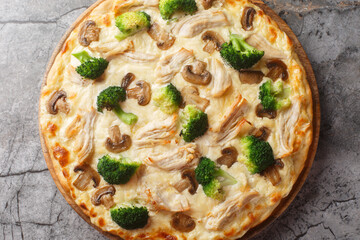 Italian white pizza with chicken, broccoli, mushrooms and cheese sauce close-up on wooden board on table. Horizontal top view from above