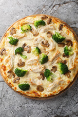 Cream pizza with chicken breast, broccoli and mushrooms close-up on wooden board on table. Vertical top view from above