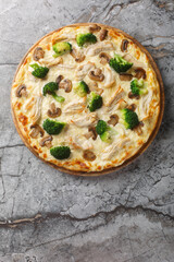 White pizza with chicken, broccoli and mushrooms closeup on the wooden board on the table. Vertical top view from above
