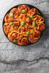 Hot pizza roll with tomatoes, cheese, Italian sausages and basil close-up in baking dish on table. Vertical top view from above