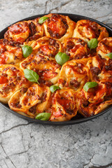 Italian pizza roll with tomatoes, cheese, sausages and basil close-up in baking dish on table. Vertical