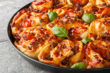 Hot pizza roll with tomatoes, cheese, Italian sausages and basil close-up in baking dish on table. Horizontal