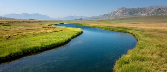  A river runs through two lush green fields, with a mountain range in the background