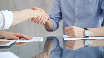 Business people shaking hands over contract agreement and financial papers at the glass table. Professional handshake, close up