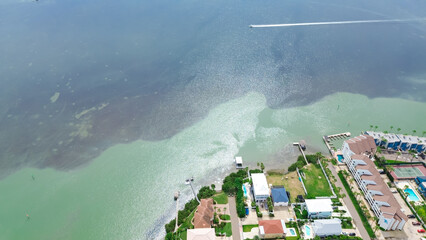 Speeding boat on shallow beach of South Padre Island near upscale neighborhood with private jetty yacht access, luxury mansion coastal houses, villas with swimming pool, palm trees, aerial view
