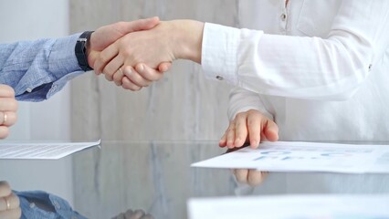 Business people shaking hands over contract agreement and financial papers at the glass table. Professional handshake, close up