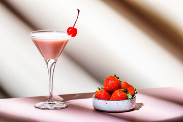 Delicious summer cocktail with vodka, liqueur, cream, strawberries and ice  with cocktail cherry. Beige background, hard light