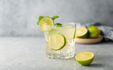 Lemonade drink with fresh lime on a texture  background. Refreshing cocktail mojito with citrus fruits, mint and ice.