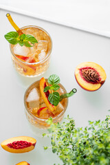 Peach lemonade with ice and mint on white background. Fresh iced tea in glasses with light from the window.