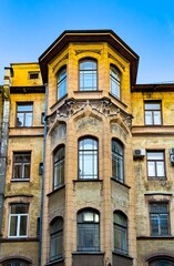 Obraz premium A detailed view of a historical residential building's facade taken from within the courtyard at a low angle during the evening. The architecture features classic elements and warm, yellow brickwork