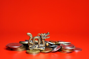 A dragon statuette with coins on a red background. Financial horoscope.