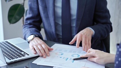 Professional businessman gestures to charts on laptop screen during corporate meeting. Business concept