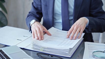 Adult businessman or auditor examining documents with magnifying glass. Professional in a suit scrutinizes financial reports, detail-focused work concept