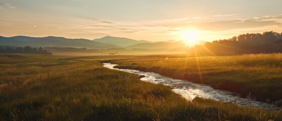  A stream runs through a lush green field, bordering another identical one covered in tall grass In the distance, mountains with peak ranges loom