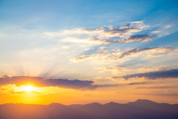The setting sun over the mountains, the beautiful sun's rays shine through the clouds, the natural background, freedom, tranquility and peace