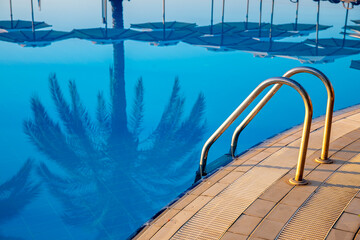 descent, ladder in the pool, reflection of palm trees in blue water, concept of rest, relaxation and calm