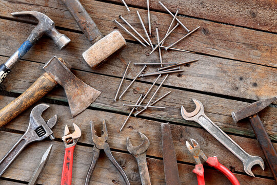 Old hand tool on a wooden surface. Adjustable wrench, spanner, axe, hammers, nails and pliers. Tools for repair and construction, top view. Construction background. Composition from an old rusty tool