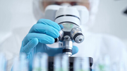 Professional scientist in protective gear is using microscope in a laboratory setting, close-up....
