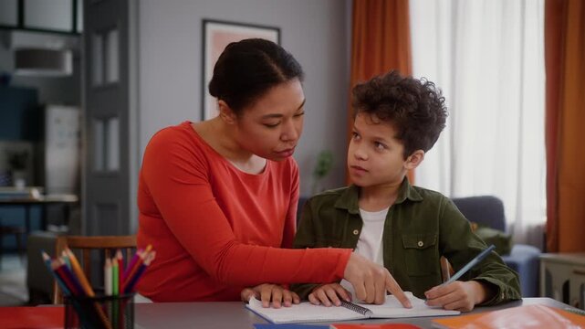 African American family caring mother mom mommy woman babysitter female helping teaching little boy support help love child kid son studying learning homework at home childcare education teach study