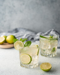 Two glasses mojito cocktail with lime, mint and ice on a light background. Trendy summer refreshing lemonade drink concept