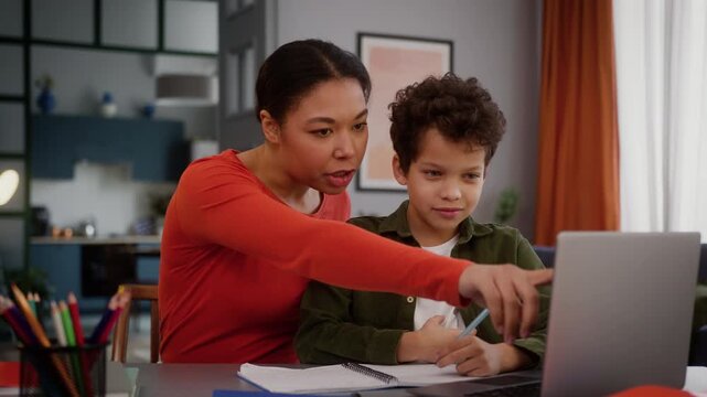 African American family caring mother mom mommy woman babysitter female helping teaching little boy help with laptop computer online course class lesson child kid son studying learning homework home