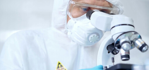Naklejka premium Professional scientist in protective gear is using microscope in a laboratory setting, close-up. Science and medicine concepts