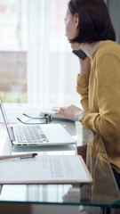 Young professional woman is talking by smartphone in modern office. Yellow blouse is passing to adult businesswoman. Business people concept