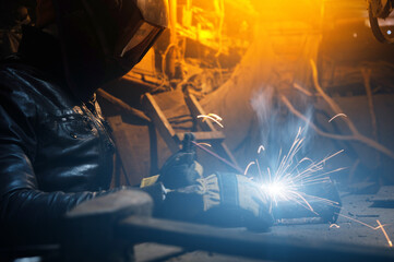 man in a welding mask welds a pipe in a dark workshop. welding smoke in the face, close-up