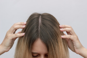 Cropped shot of a young blonde woman showing regrown hair roots on a grey background. The result is months after hair discoloration with the airtouch technique. Beauty concept