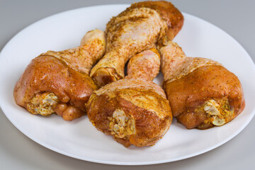 Raw chicken drumsticks with spices on dish on gray background