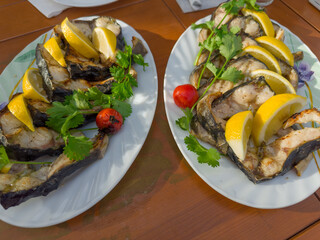 Grilled steaks of sturgeon with lemon and greens on plates