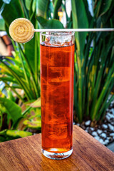 Red cocktail in highball glass filled with lot of ice. Vibrant red color contrasts with clear, frosty ice cubes, inviting appearance. Lollipop adds playful colorful touch, positioned on top of cocktai