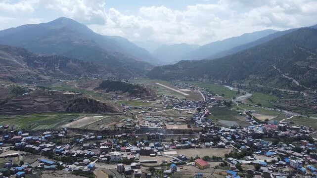 Aerial view of Jumla Bazar, a town in western Nepal surrounded by mountains. The town's buildings are spread across terraced fields, with a small river running through the valley.