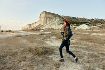 Woman in hat and jeans walking in desert with mountain in background