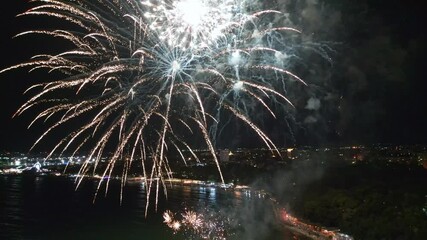 Spectacular fireworks display illuminating the night sky over a vibrant city waterfront, with reflections shimmering on the water below. Perfect for celebrations and festive events. Reverse video