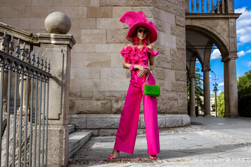 Obraz premium Spring summer fashion. High fashion model. Glamour, stylish elegant woman in pink jumpsuit and big hat. Female model in stylish look in the city. Outdoor shoot.