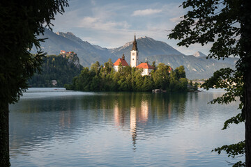 Fototapeta premium Church of the Mother of God with castle and mountains in background, Lake Bled, Slovenia