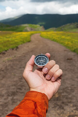 Compass in hand against the background of a mountain road, vertical photo. Choosing a path in...