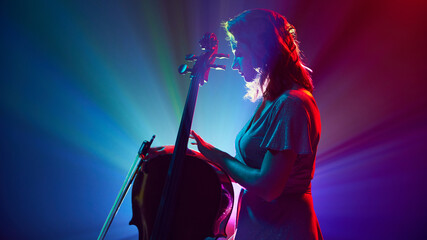 Silhouette of artistic woman, musician standing on stage with musical instrument, double bass in vibrant stage lights. Concept of classical and modern music, entertainment, jazz. Ad