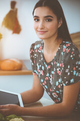 An attractive young dark-haired woman chooses the recipe for a delicious meal while sitting at the table in sunny kitchen