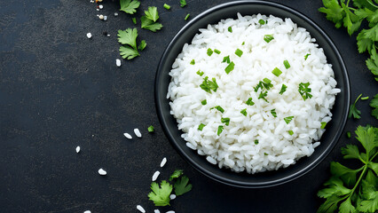 Bowl of white rice on a black background, top view, with coriander leaves scattered around the bowl.