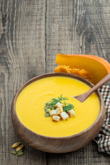 Pumpkin cream-soup served with croutons in wooden bowl on rustic table