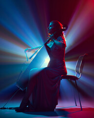 Silhouette of young woman, musician playing cello solo on stage in dramatic spotlights and smoke....