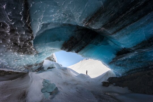 Winter landscape view of a hiker standing on a snow-covered rock, exploring an ice cave