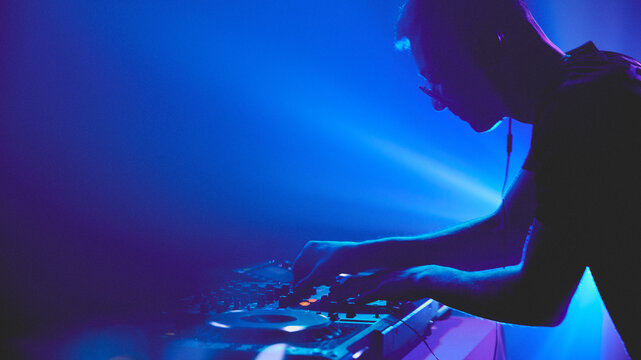 Symphony of light and sound. DJ commands deck, his movements synchronized with shifting spotlights that paint dancefloor. Concept of modern music and technology, party, disco, nightlife.