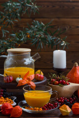 yellow tea with sea buckthorn berries in a glass teapot. Decorated with physalis and autumn pumpkins, sea buckthorn tea